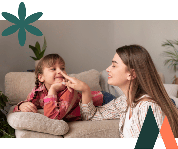 Mother and child sitting together on a couch during a supportive therapy session, both sharing a warm smile.