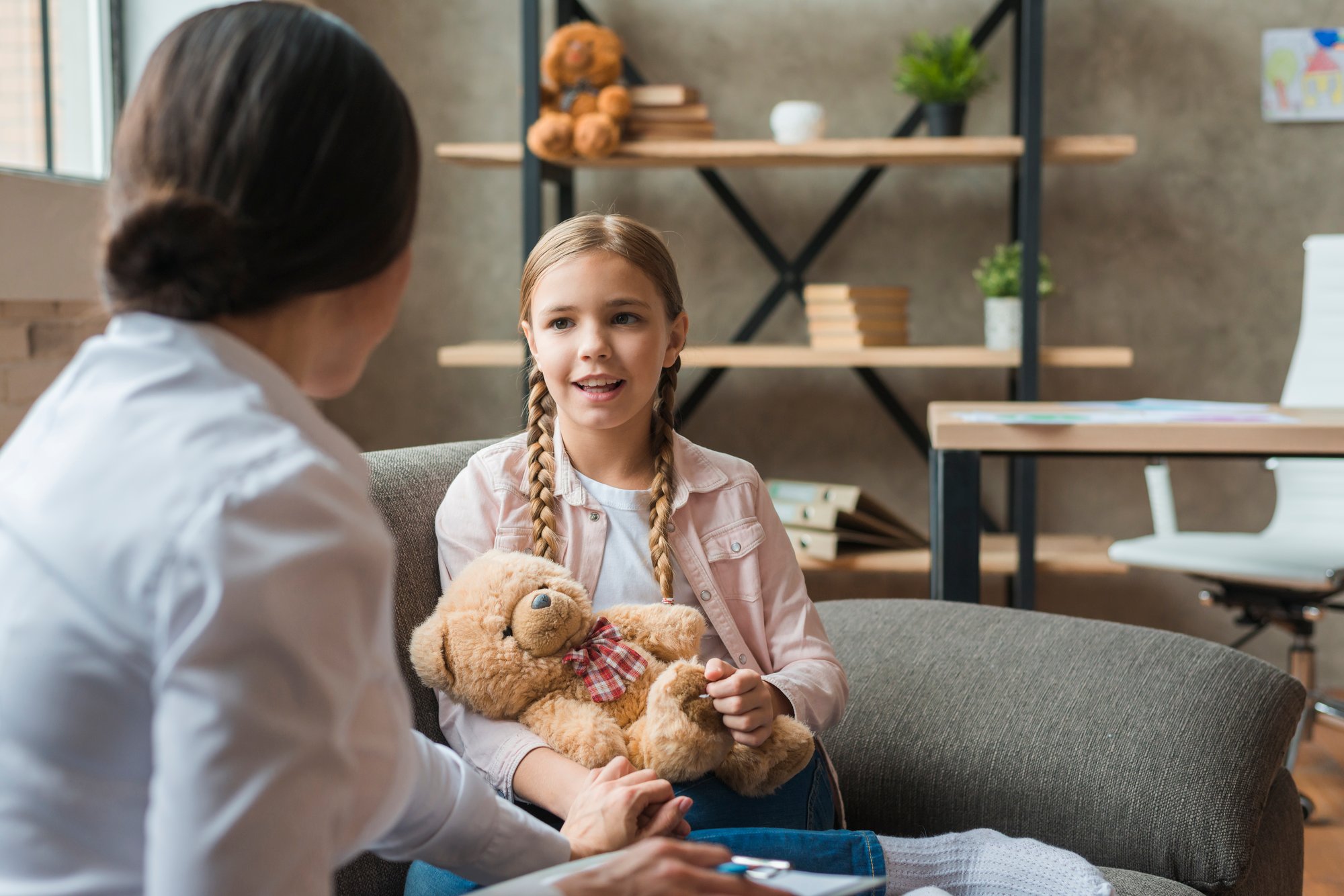 Child seated across from a therapist at a small table, speaking and gesturing expressively during a session.